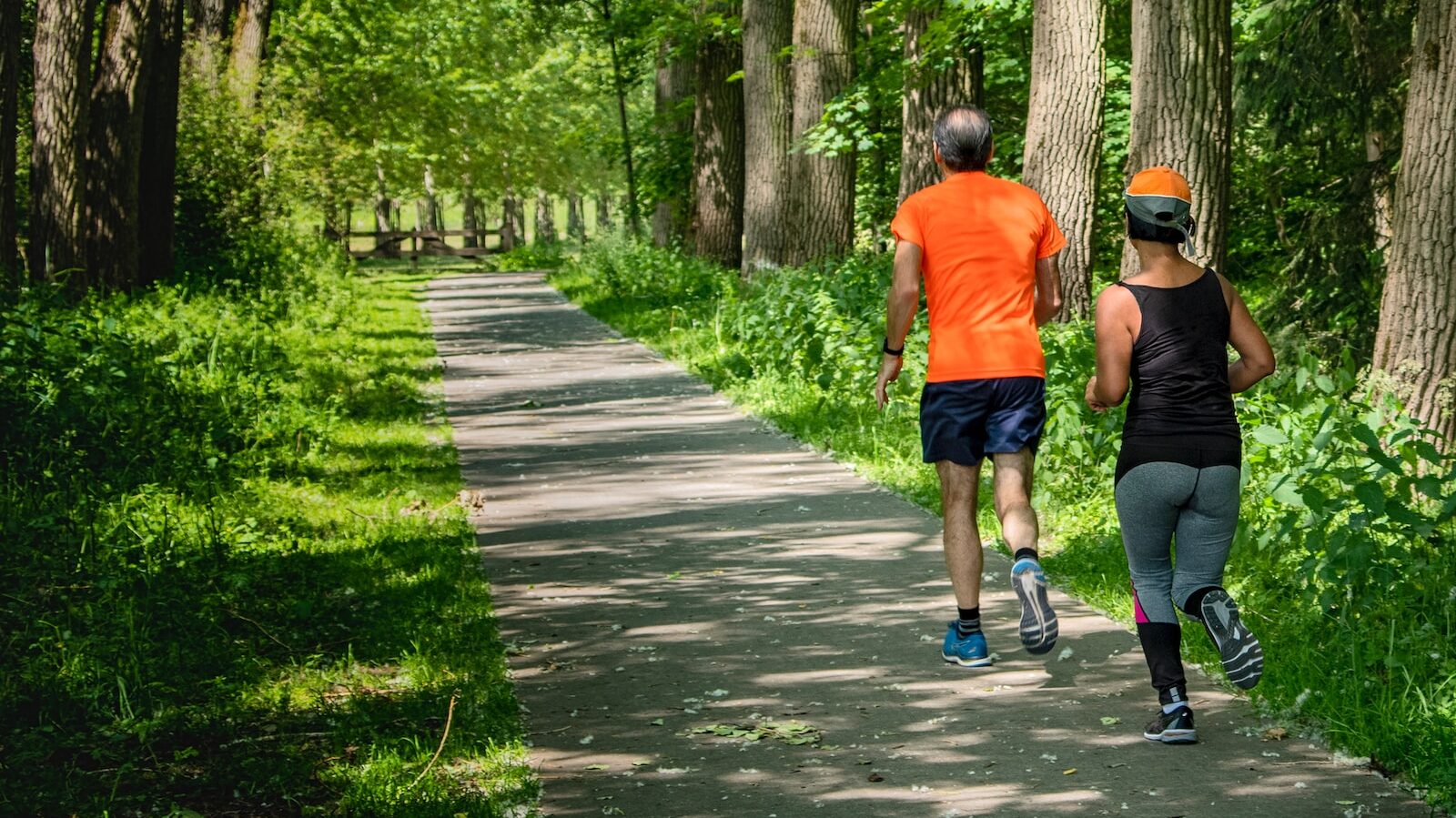 man in orange t-shirt and gray pants with blue shoes walking on pathway