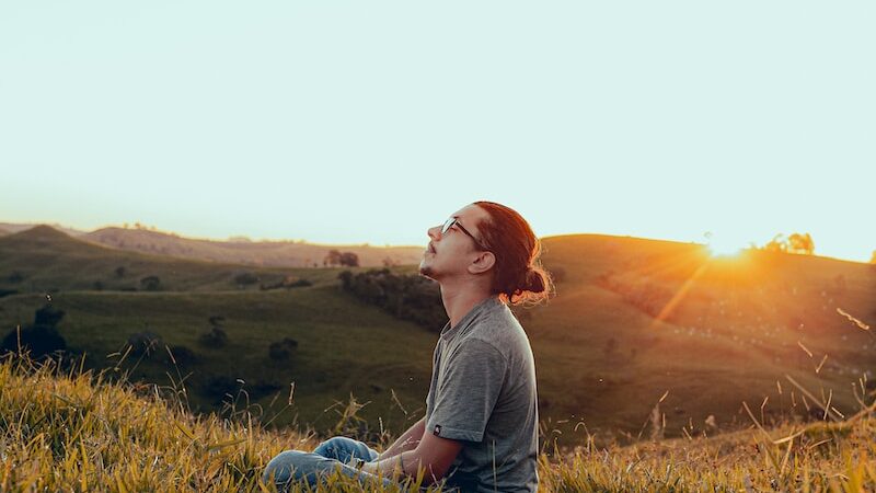 man in white shirt sitting on green grass field during sunset